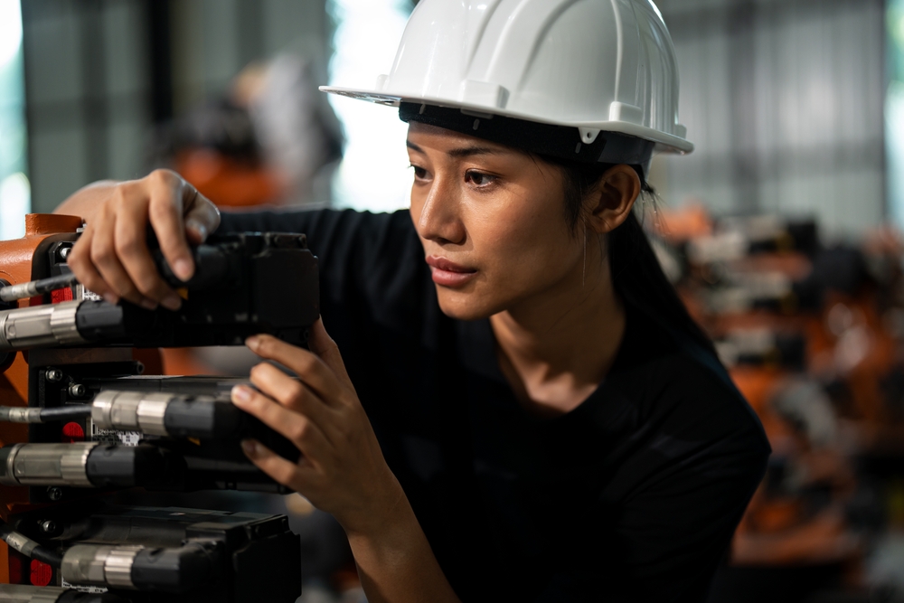 Female foreign worker wearing a safety helmet operating machinery in a Japanese factory